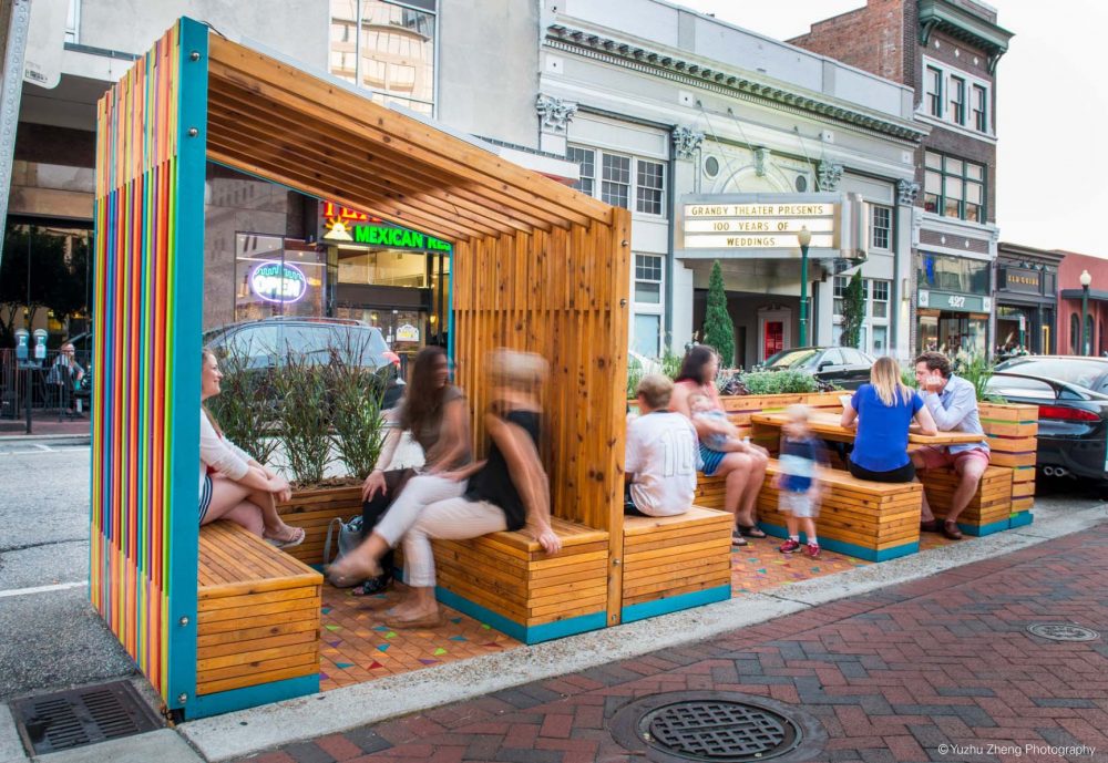 Parklet in legno colorato, parzialmente coperto, con persone sedute ai tavoli